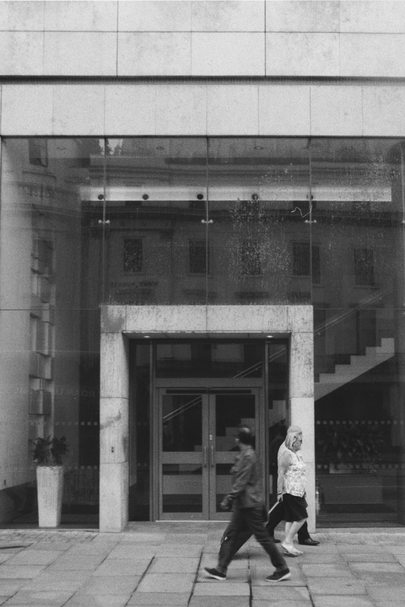 Black and white image of people walking past a modernist building